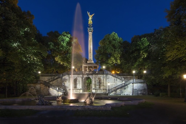 Der goldene Friedensengel wird nachts in MÃ¼nchen angeleuchtet, sowie der Springbrunnen davor. 